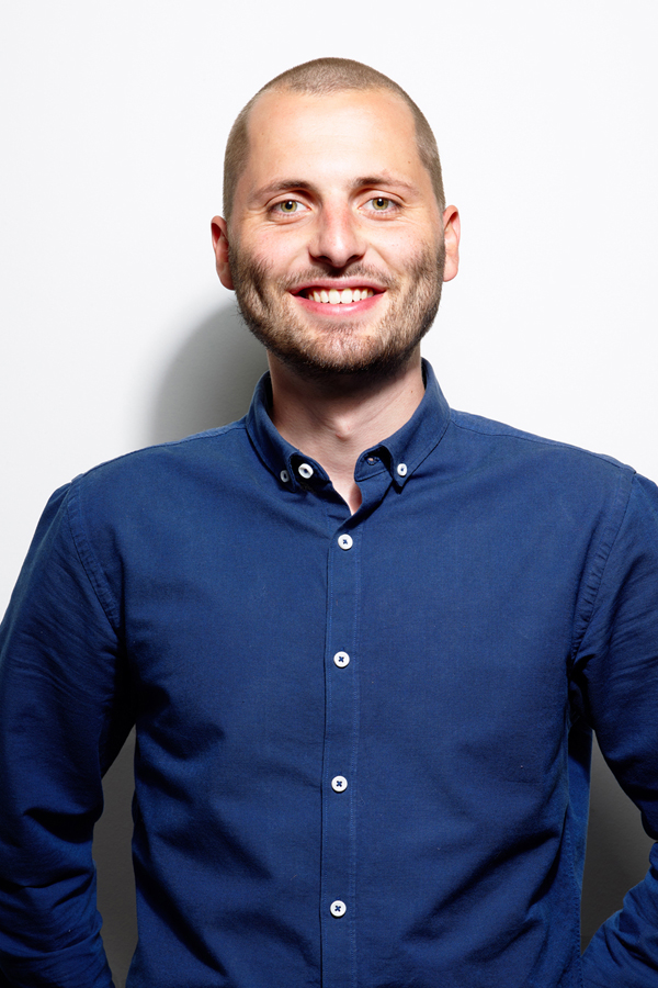 Employee photo of Corbinian Ruckerbauer. He is wearing a blue shirt and standing in front of a white wall.