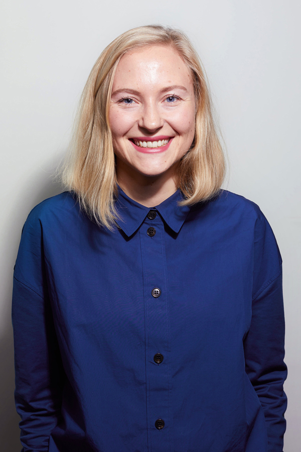 Staff photo of Julia Christina Hess. She is wearing a blue blouse and standing in front of a white wall.